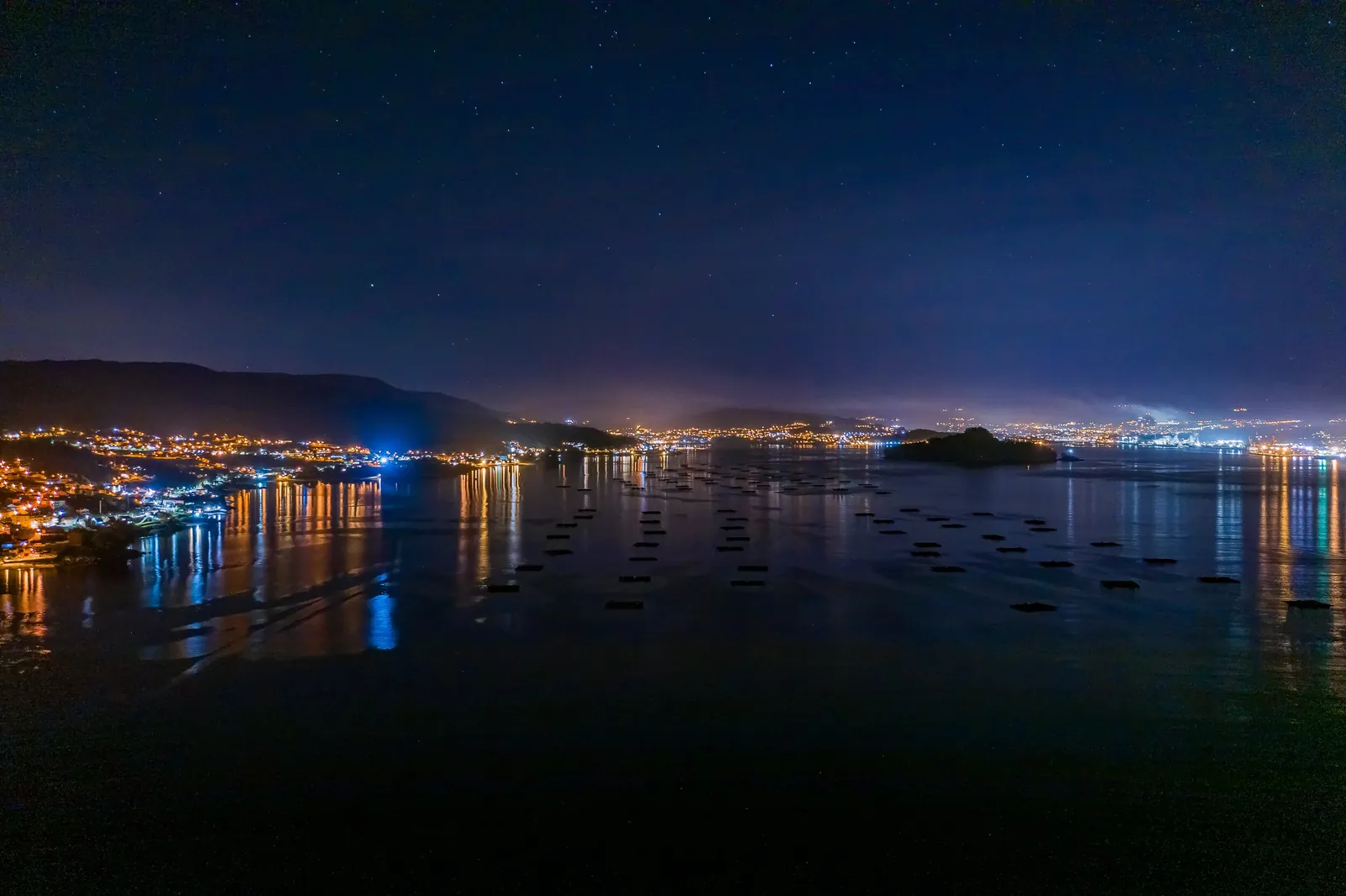 Fotografía aérea nocturna de una bahía iluminada. MAC Estudio